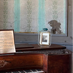 Vintage piano with sheet music and a small framed picture against a patterned wall.